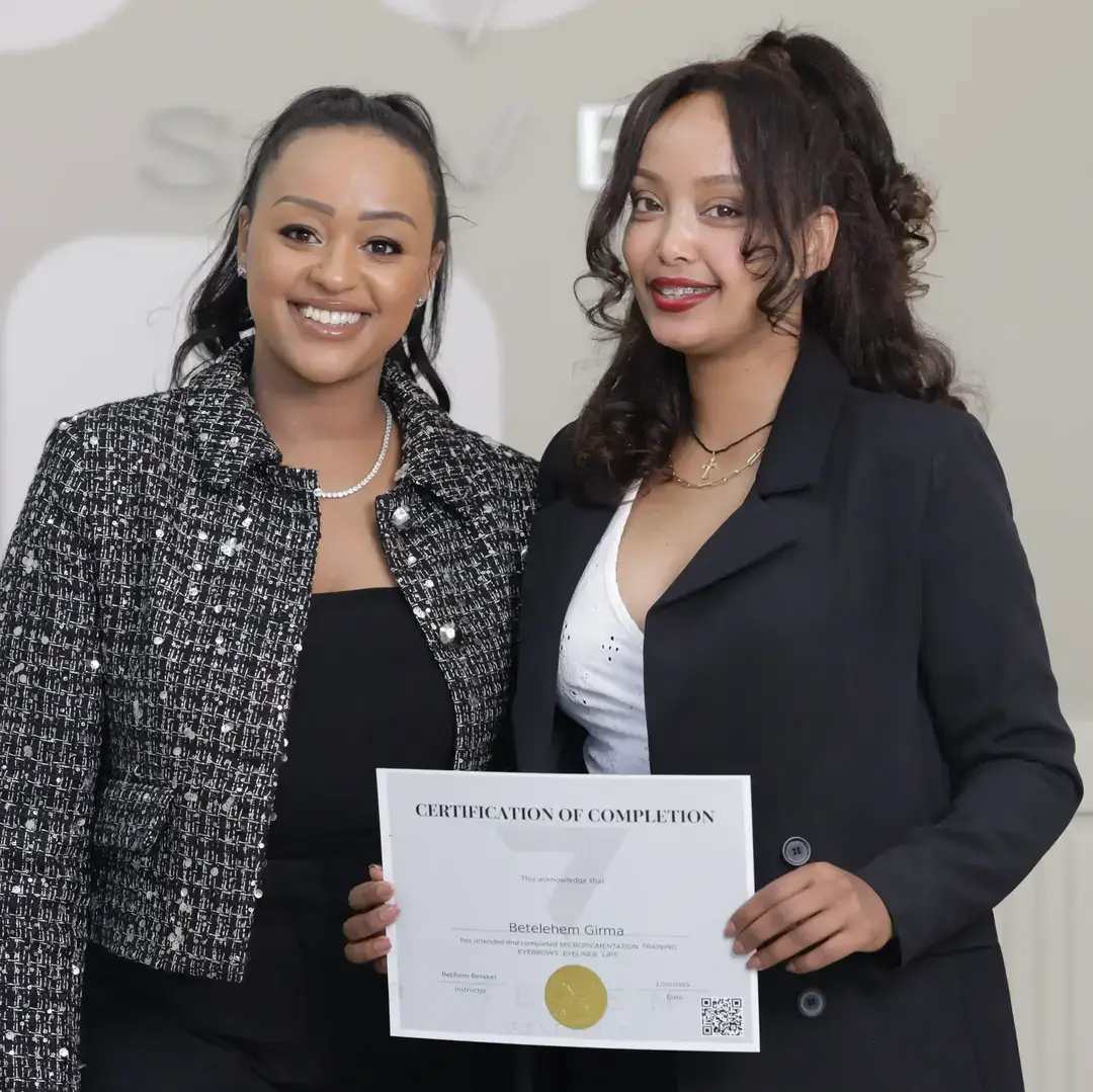 Permanent Makeup Certification at Seven Aesthetics: Teacher Betlehem Bereket with student Betelehem Girma holding her certificate of completion after completing the course.
